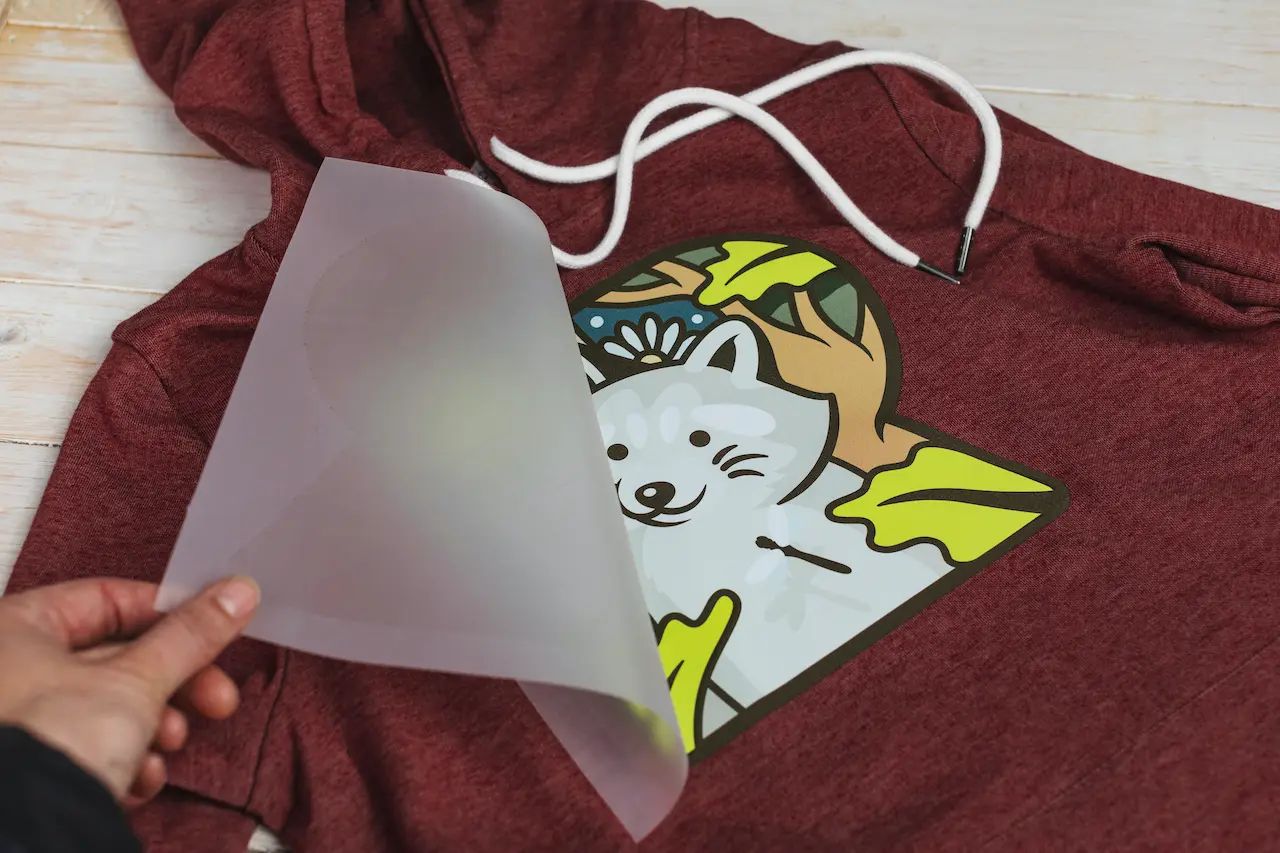 Carrier film being peeled from a colorful transfer on a hoodie